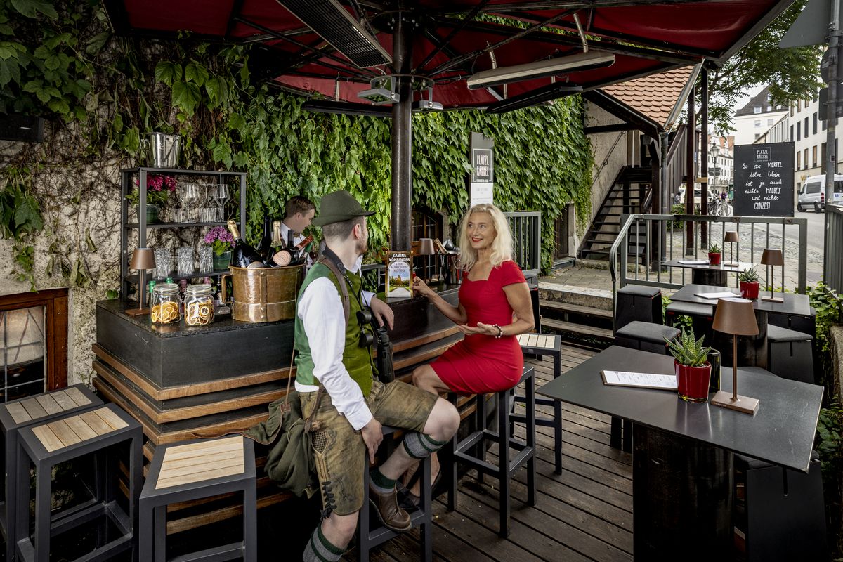 A man in a traditional Bavarian costume sits with a blonde lady in a red dress at the bar in Platzl Karree.
