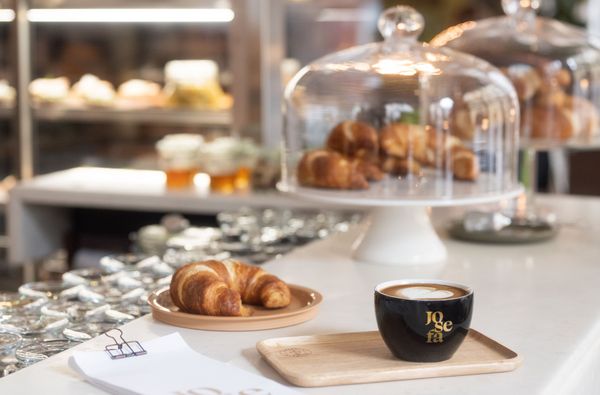 A few croissants and a cappuccino in a cup of the at the Josefa on top of a counter .